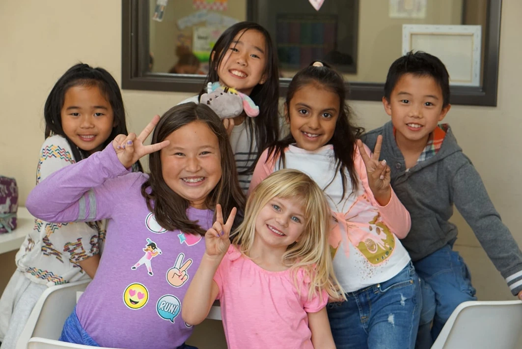 Six smiling, diverse students giving peace signs in an engaging our after-school programs